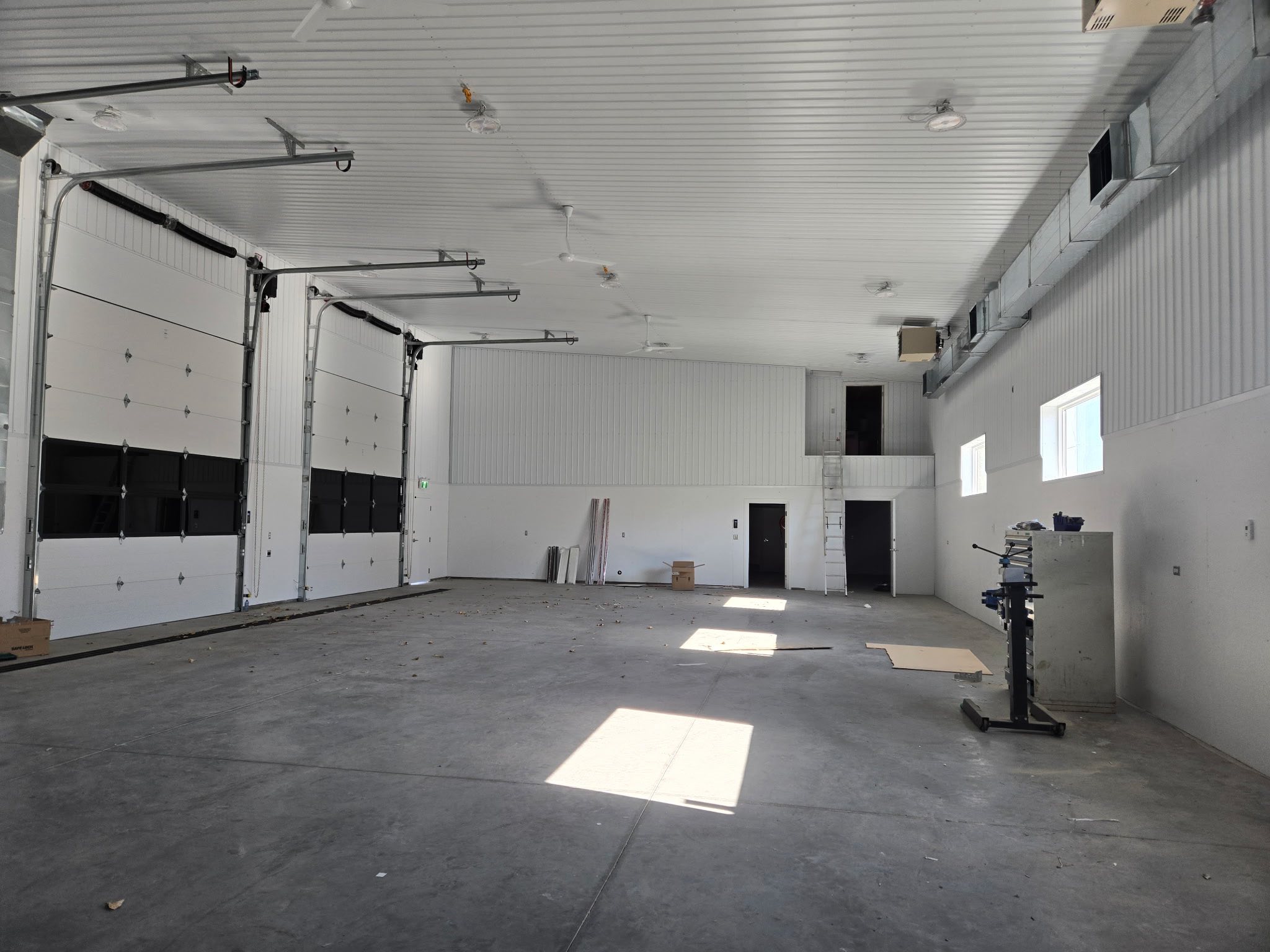 Spacious, clean garage interior with high ceilings, large closed overhead doors, and bright windows. Reflective concrete floor. Industrial atmosphere.