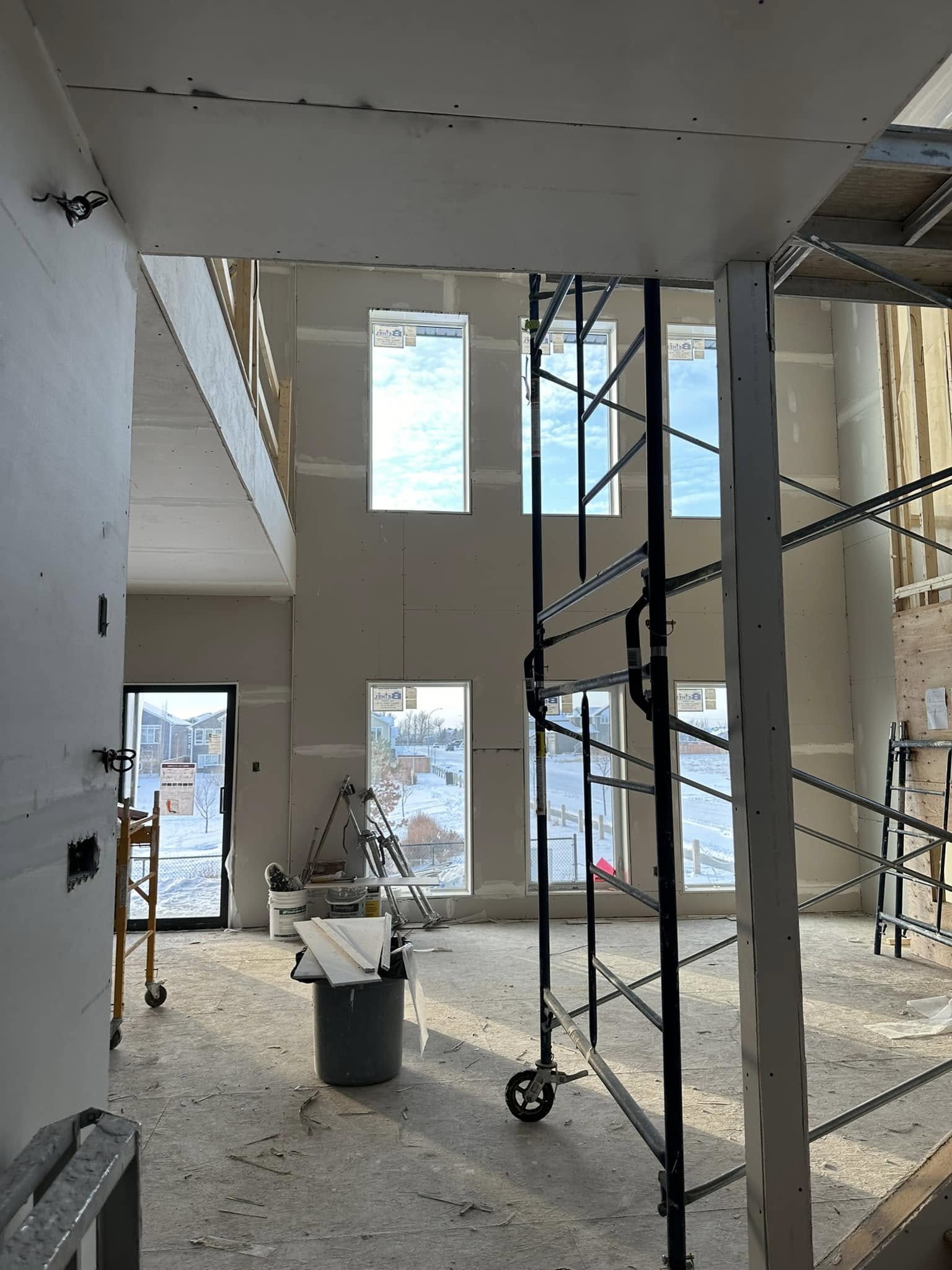 Construction site of a house with large windows letting in light. Scaffolding and tools are visible inside, conveying a sense of ongoing work.